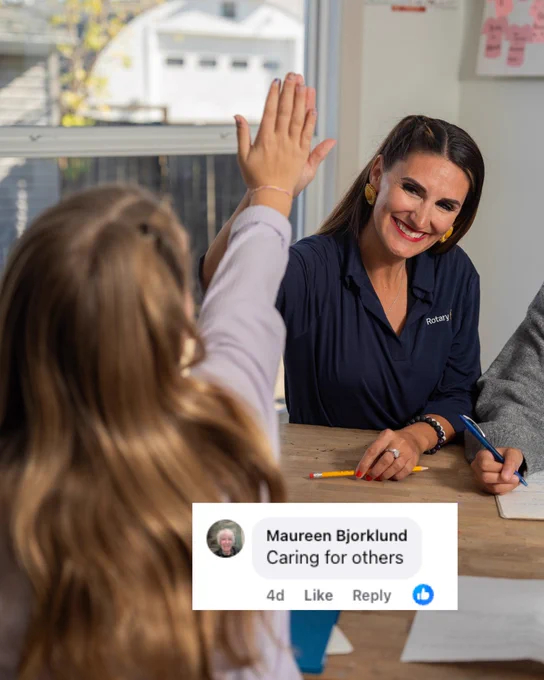 A Rotary member smiling at a child raising their hand in a classroom setting, with a social media overlay indicating a comment stating 'Caring for others.'