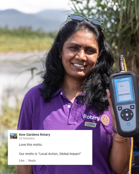 Member of a Rotary Club holding a scientific device, standing outdoors with greenery in the background. The person is smiling and wearing a purple Rotary shirt with the slogan 'Esrag.'