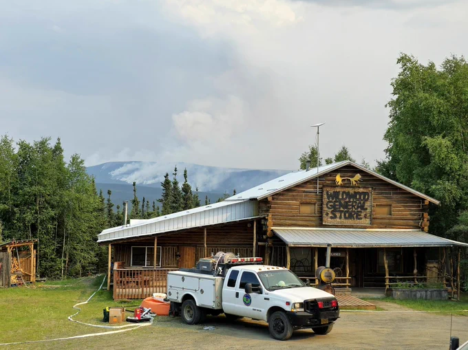 Structure protection in Alaska. A wildfire burns in the timber in the background. Photo by BLM Alaska Fire Service. 