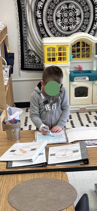 studend standing at a table using a dry erase marker writing his name on a laminated notebook