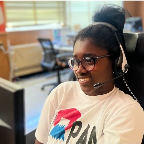 A young woman in a wheelchair, sporting a t-shirt and headphones, actively using speech-to-text for writing.