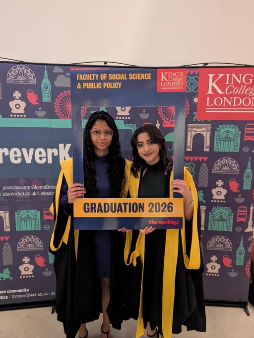 Two graduates smiling as they pose with a frame with the words 'graduation 2026' on it.