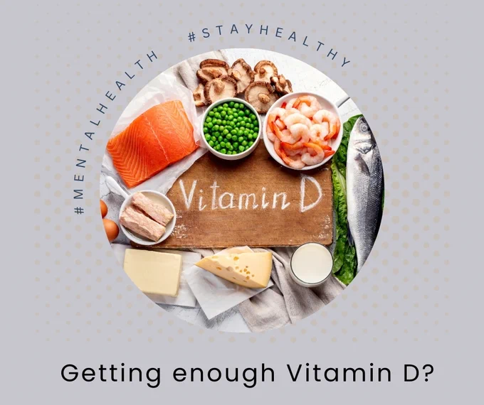 A photograph of a cutting board with Vitamin D written on it surrounded by cheese, fish, milk, shrimp, salmon, mushrooms, and peas.