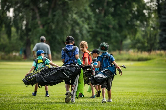 A group of boys carry golf bags across the green