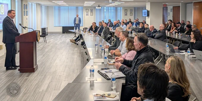 A person is giving a presentation at a podium to a group of attentive listeners in a conference room setting.