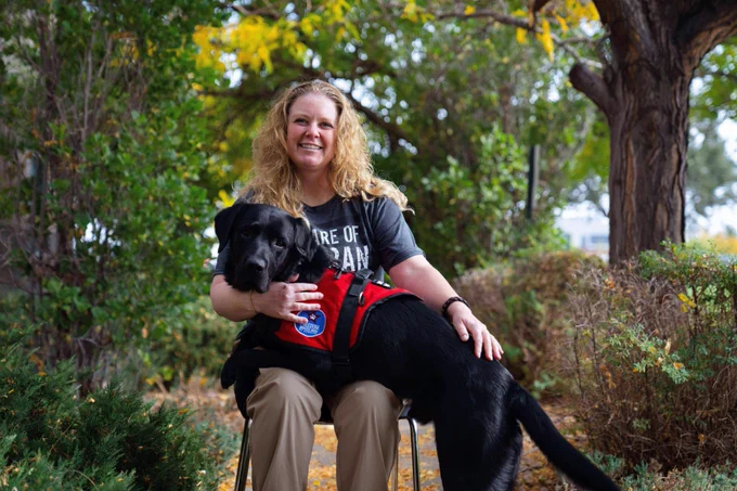 Ashleigh sits with her assistance dog Montana, a black labrador, lying across her lap and applying deep pressure therapy.