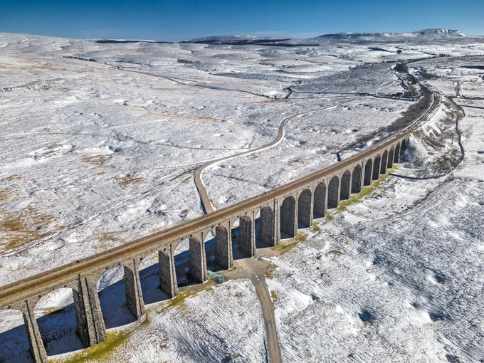 Long stone railway viaduct stretching across a snowy landscape under a clear blue sky.
