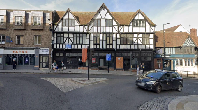 Modern colour photo of the same street corner, now with a black-and-white timber-framed building, a taxi, pedestrians, and updated signage.