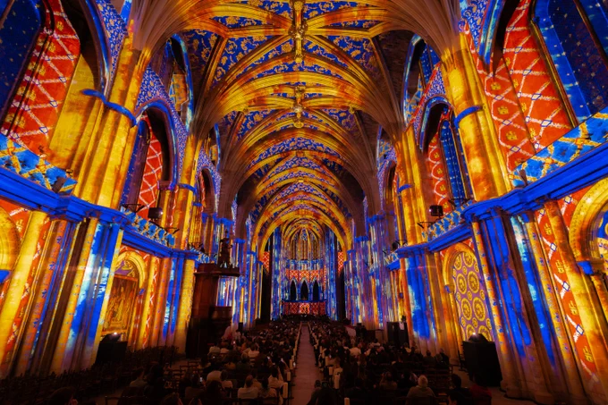 Cathedral interior with columns and vaulted ceiling lit up with red, blue and yellow projections.