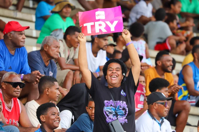 A woman in the stands smiles and holds up a sign that says 'Try'.