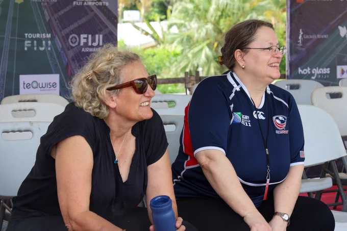 Ambassador Damour smiles while watching the game seated next to another spectator.