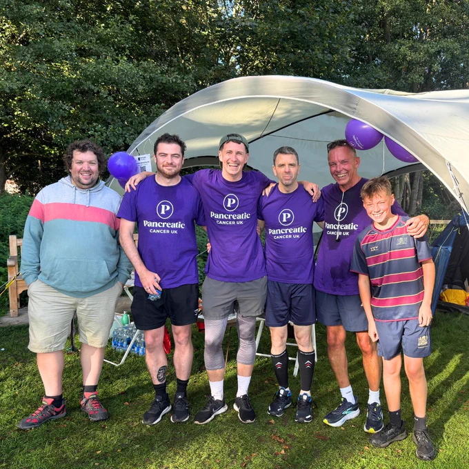 A group of people in Pancreatic Cancer UK t-shirts stand together in front of a gazebo, smiling at the camera.