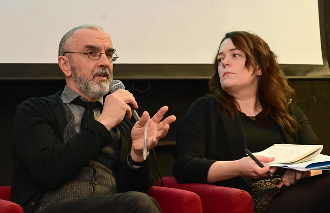 Dr Roddy Flynn and Dr Dawn Wheatley (Dublin City University) engaged in a discussion, one holding a microphone and the other taking notes in a notebook.