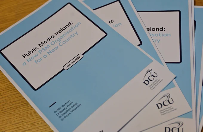 Stack of blue booklets titled 'Public Media Ireland: a New PSM Organisation for a New Country' on a wooden surface.