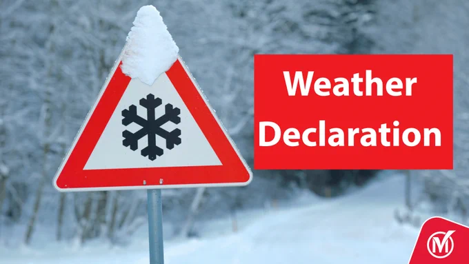 Triangular road sign with snowflake symbol covered in snow, with the words weather declaration on it.