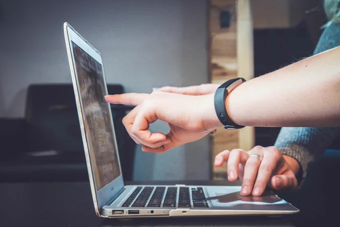 Two hands interact with a laptop; one points at the screen, the other types on the keyboard. 