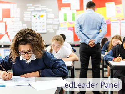 Students focused on writing at desks while a teacher observes in a colorful classroom setting.