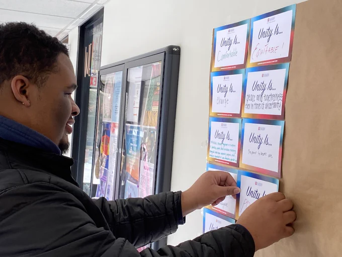 A Duquesne community member places their "unity is" response card on the wall.
