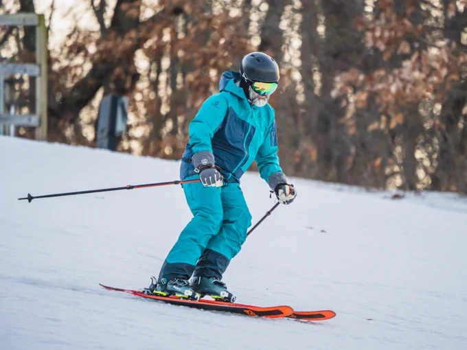 A person in a bright blue ski suit and helmet skiing down a slope with trees in the background.
