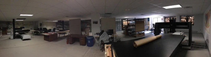 Wide view of a spacious basement workshop with various tables, storage shelves, and equipment scattered around the room.