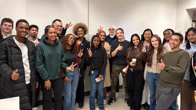 Group of smiling students posing with Dean Andrade in a classroom setting, some making peace or thumbs-up gestures.
