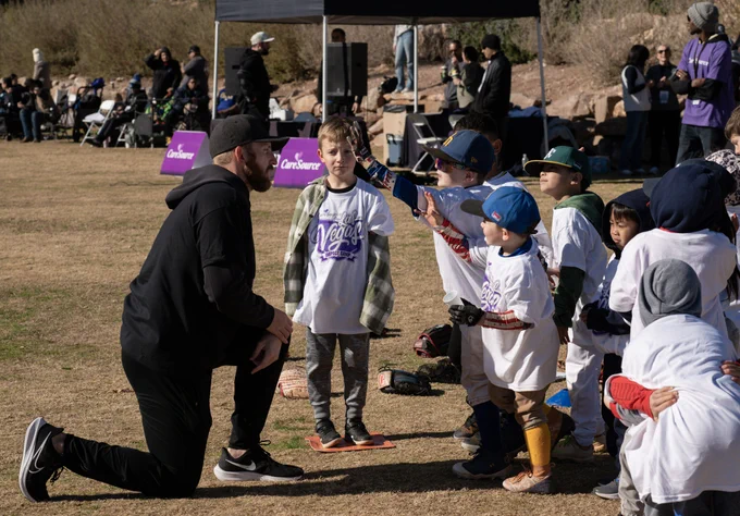 Group of children in sports uniforms interacting with an adult at an outdoor event.