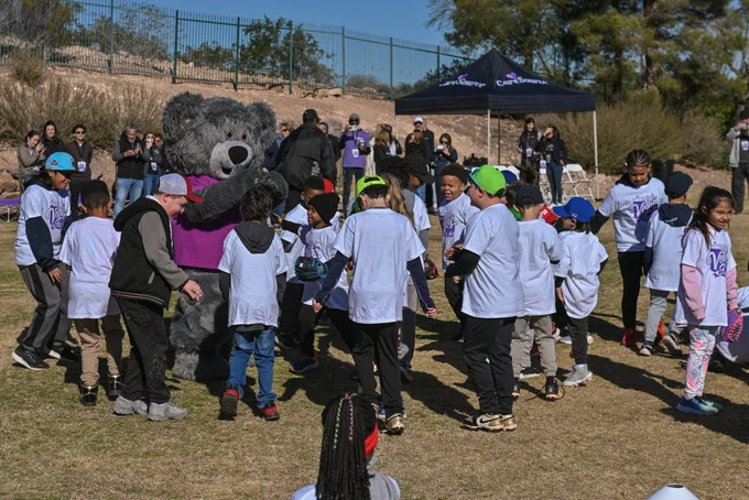 A group of children in white shirts engaging in an outdoor activity, interacting with Cuddles.