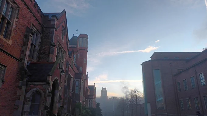 A building tower emerging from fog on a winter morning, framed by an old, Victorian building on the left (Lanyon Building, Queen's University Belfast) and modern building on the right.
