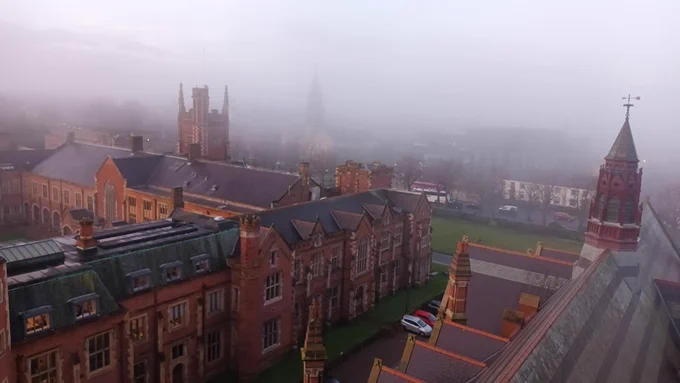 Aerial view of old, Victorian buildings (Lanyon Building and Graduate School, Queen's University Belfast) with background buildings shrouded in fog.