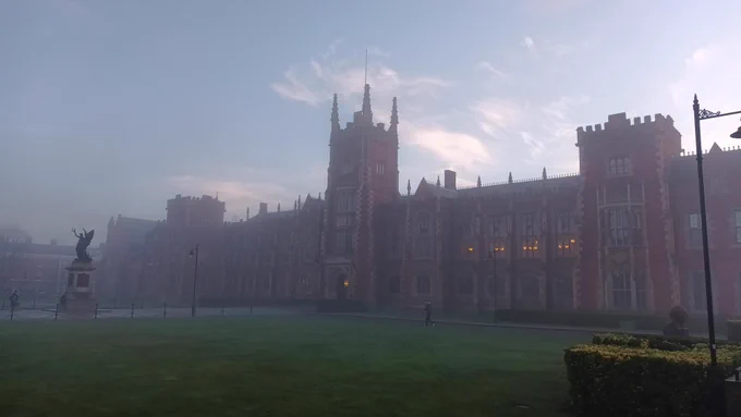 An old, Victorian building (Lanyon Building, Queen's University Belfast), war memorial and front lawn on a foggy winter morning
