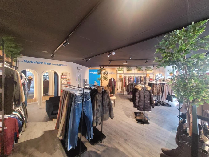 Another view of the inside of the new Yorkshire Cancer Research shop in Skipton. The words "For a Yorkshire free from cancer" is visible on the wall, as well as a variety of clothing and accessories.