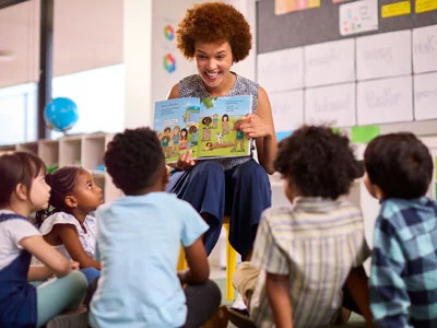 Teacher reading a colorful storybook to a group of attentive young children seated on the classroom floor.