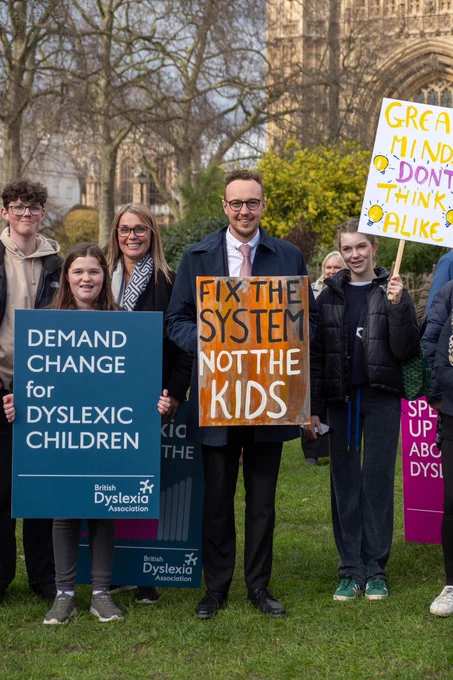 Adam Dance MP stands with children and adults at a rally, holding signs calling for better support for dyslexic children.