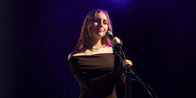 UWM Arts student Ariel Marks is singing on a dimly lit stage.