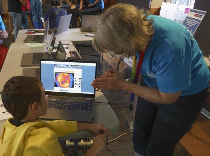 An educator points to a laptop screen as a child watches.