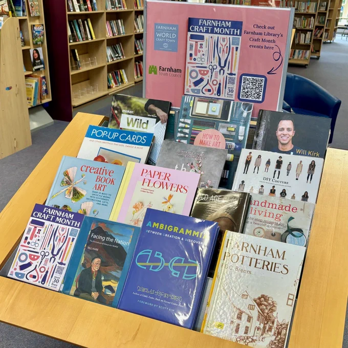 A display of arts and craft books in Farnham Library, with an image of the Farnham Craft Month brochure on a poster above.
 