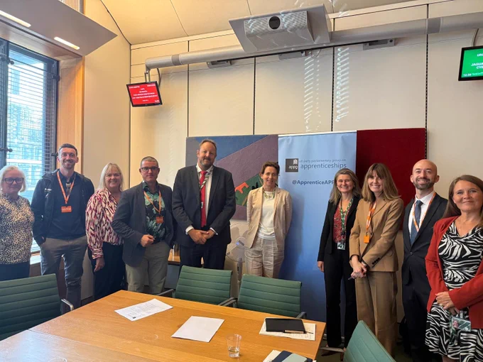 Toby Perkins MP, other parliamentarians, and stakeholders part of the APPG for Apprenticeships in a meeting room in Parliament, standing in front of a sign for the APPG for Apprenticeships.