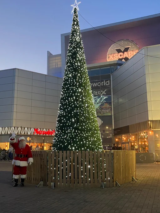 Christmas tree illuminated with white lights next to Santa Claus, outside the Xscape Yorkshire. 