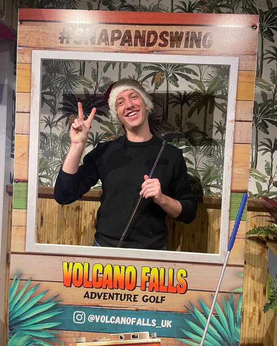 Person posing with a peace sign inside a frame labeled "#SnapandSwing" at Volcano Falls Adventure Golf.