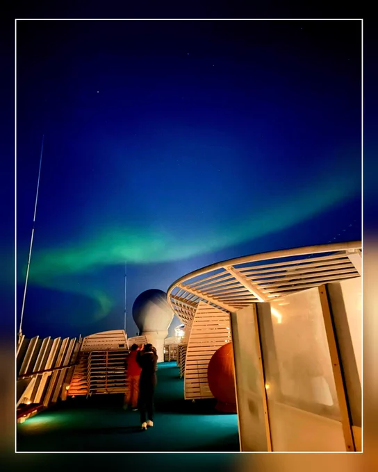 Pooldeck der Aida Luna bei Nacht mit Polarlicht darüber. Passagiere fotografieren in den Himmel.