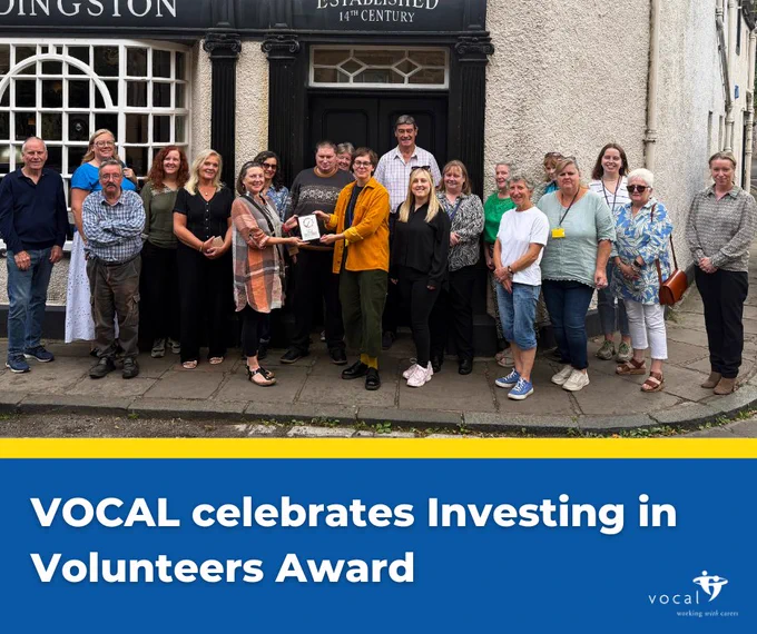 Vocal staff and volunteers hold the investing in volunteers award plaque.
