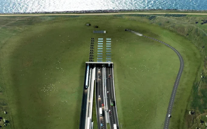 Computer generated aerial view of the Fehmarnbelt tunnel, showing vehicles approaching the tunnel entrance, surrounded by expansive grassy fields and a coastline in the background.