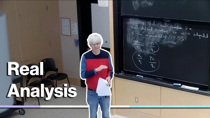 A person with white hair stands in front of a blackboard filled with mathematical equations, holding papers and wearing a red, blue, and white shirt. The text "Real Analysis" appears overlaying the image.