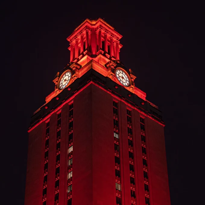 The University of Texas Tower illuminated in burnt orange at night.