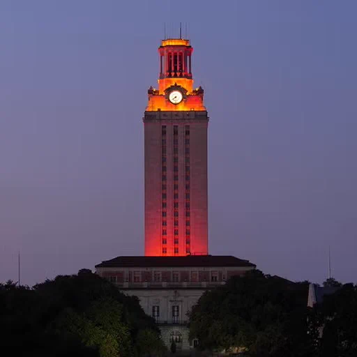 The University of Texas Tower illuminated in orange against a twilight sky, flanked by nearby buildings.