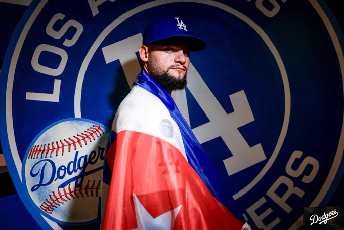 A photo of Andy Pages posing with the Cuban flag in front of a Dodger mural.