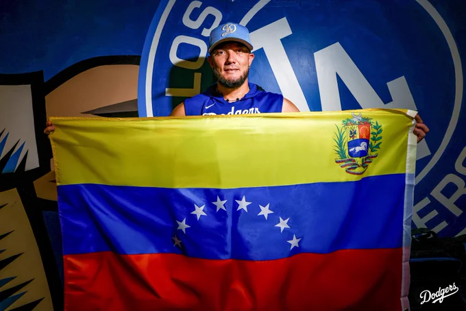 A photo of Miguel Rojas posing with the Venezuelan flag in front of a Dodger mural.
