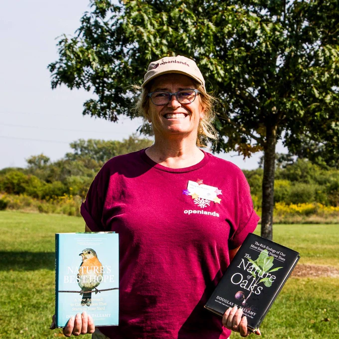 Openlands Ecologist Mary Fortmann is standing in front of a tree holding 2 books. "Nature's Best Hope" and "The Nature of Oaks"