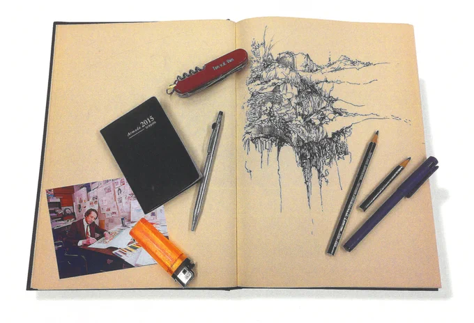 Een opengeslagen tekenboek met daarop potloden en pennen, een zakagenda 2015, zakmes met gravure "Ton v.d. Ven", een aansteker een een foto van Ton aan zijn bureau