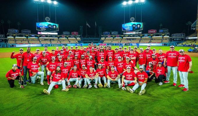 The Phillies gather for a group photo on the field at Dodger Stadium. They are all wearing red NL East Champions shirts.